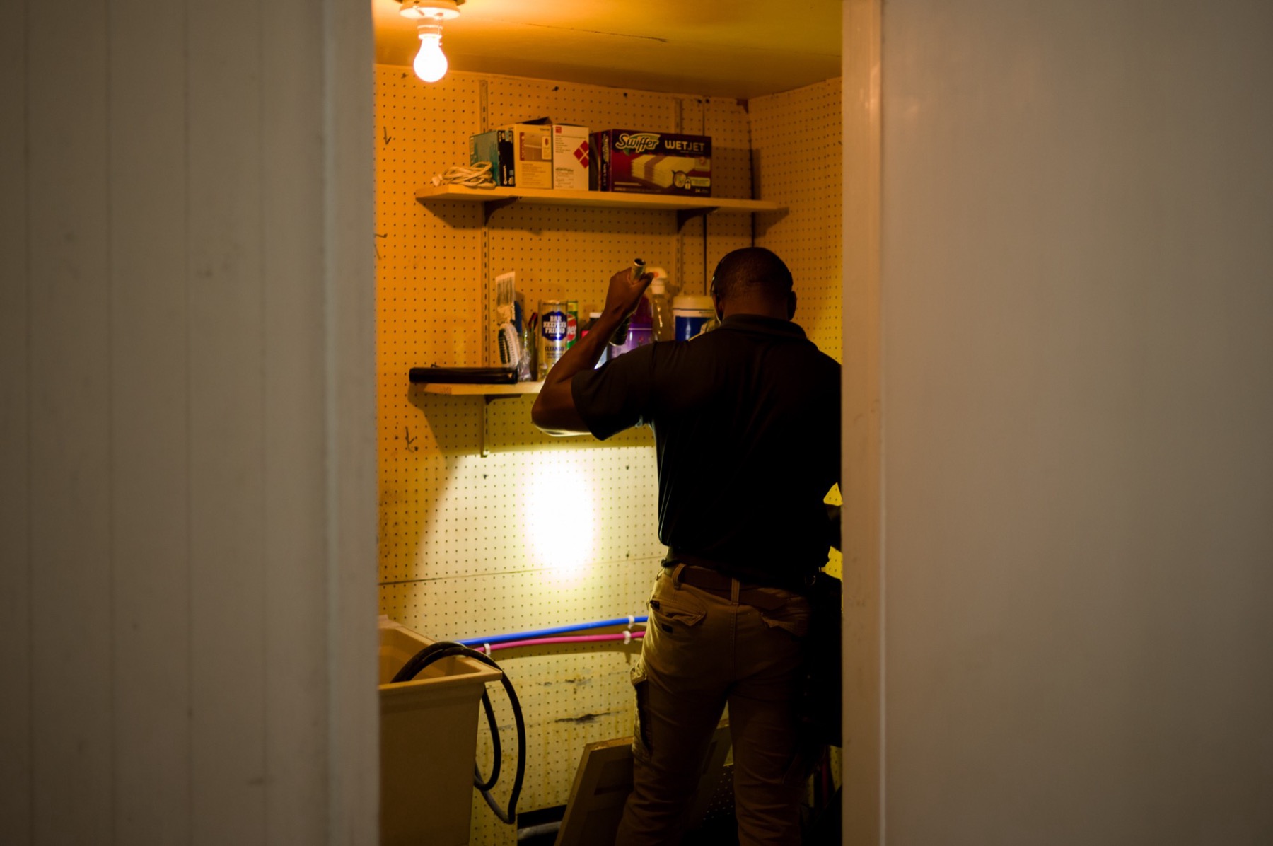 Inspector using a flashlight to check walls and plumbing inside a utility closet