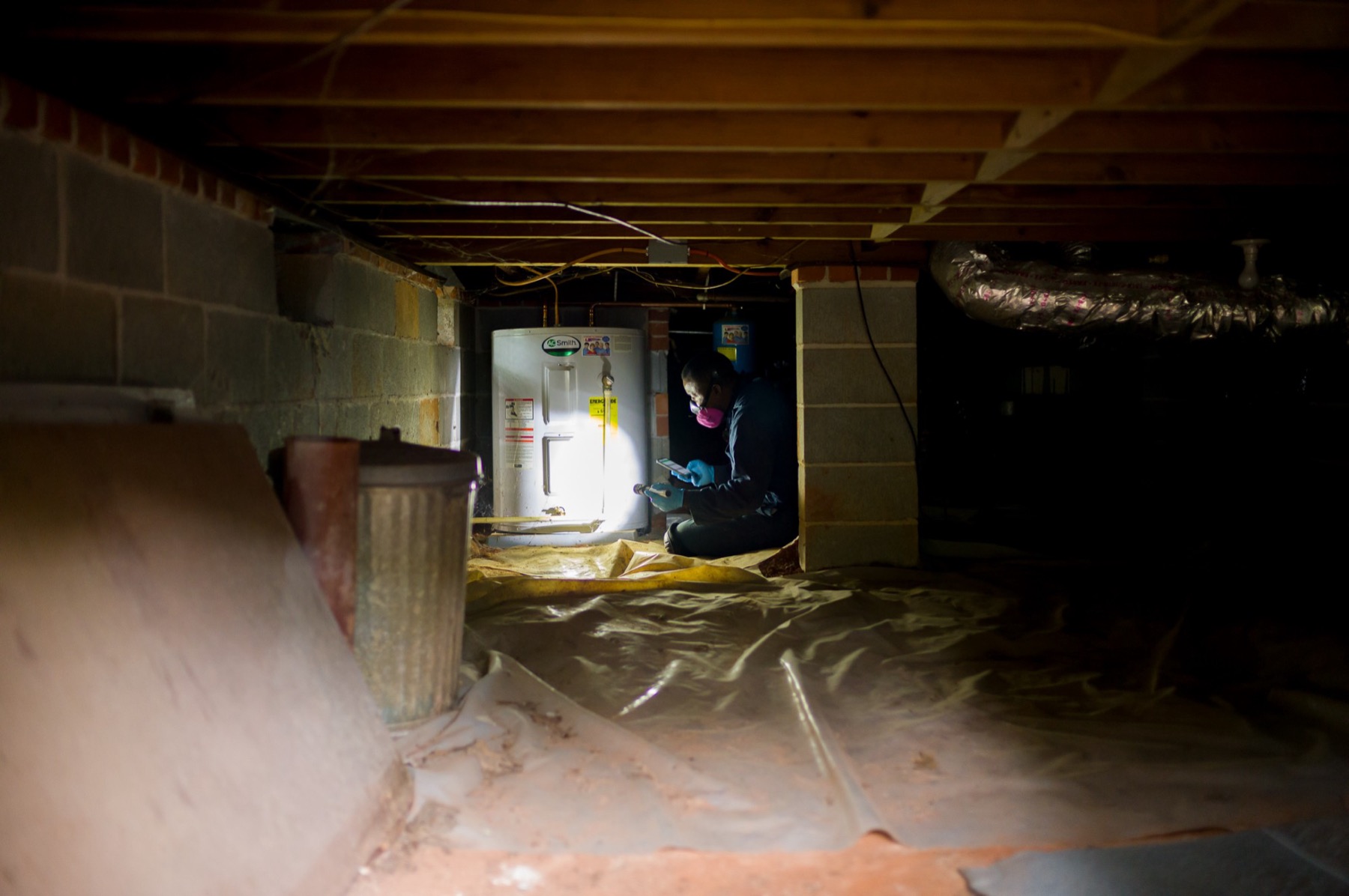 Home inspector in a respirator examining a water heater and floor framing in a crawlspace in Athens, Georgia