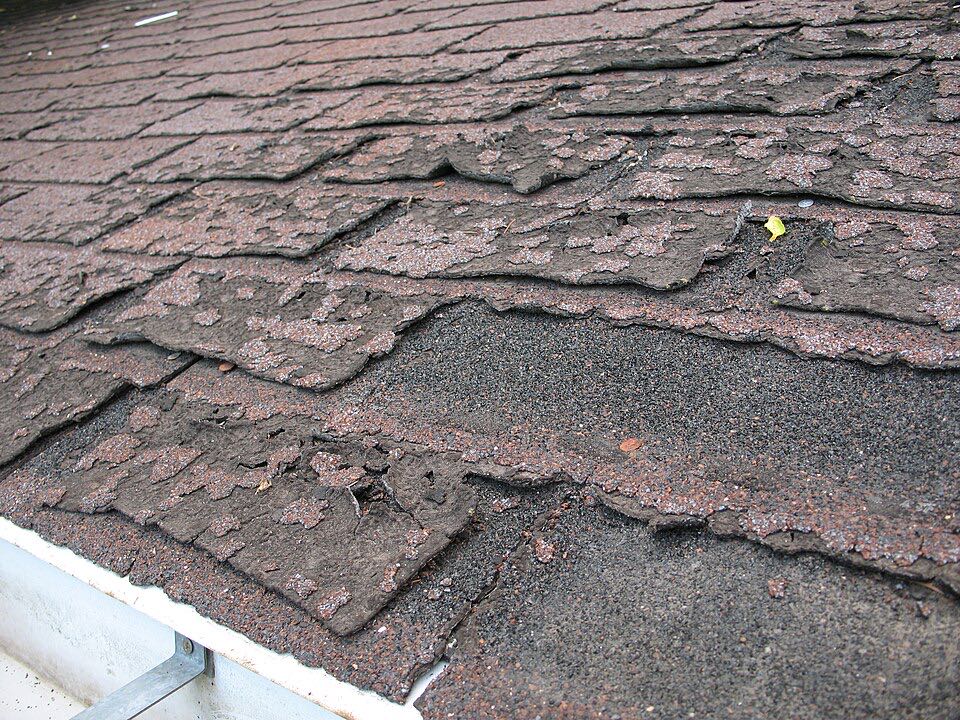 Worn asphalt shingles with lost granules, cracked and curling edges